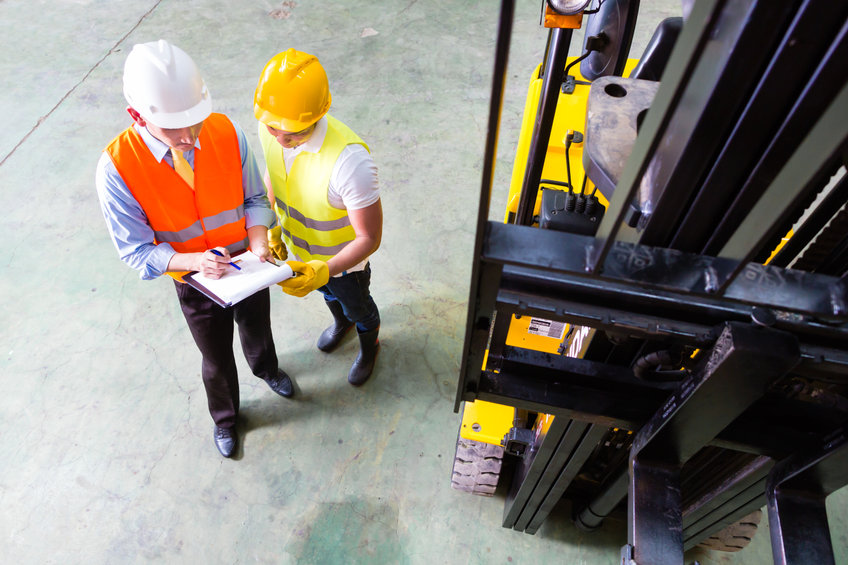 Asian fork lift truck driver discussing checklist with foreman in warehouse